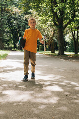 Outdoor activities for children. An upset young boy in sunglasses stay with a skateboard in a public park. Caucasian schoolboy on a walk. Front view