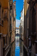 Touristic gondola in narrow grand canal between buildings in Venice, Italy. On boat is a gondolier with a long oar. Azure water and mesmerizing blend of tourists, gondolas, and narrow streets. 