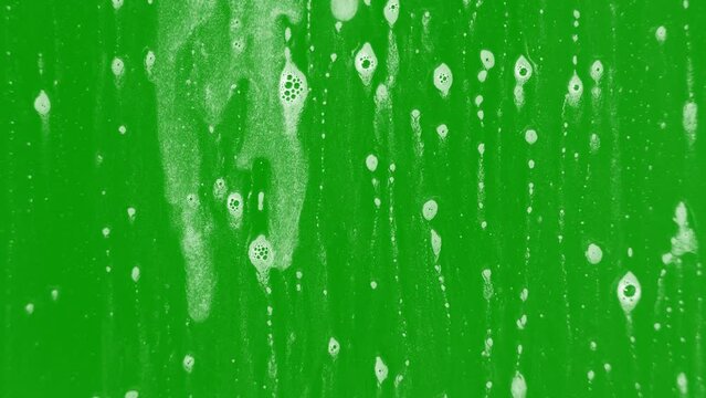 Foam dripping on glass with a greenscreen background with bubbles