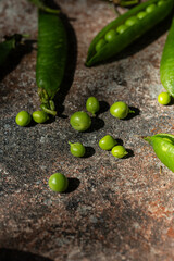 Fresh green peas in pods on stone surface in harsh sunlight.