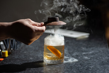 Bartender hands making cocktail with ice and orange zest with smoke 