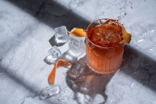 Orange cocktail splash with zest on marble table and shadows hard light