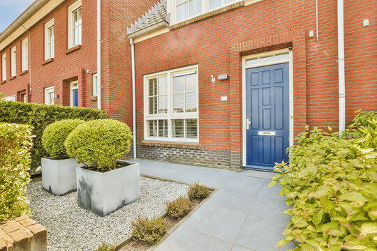 a red brick house with blue front door and plants in the fore - image is taken from an angleer's perspective