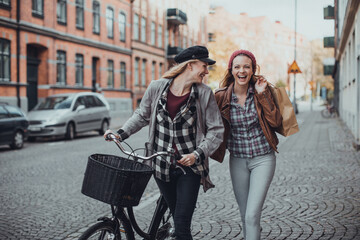 Obraz na płótnie Canvas Young women pushing their bicycles on a city street