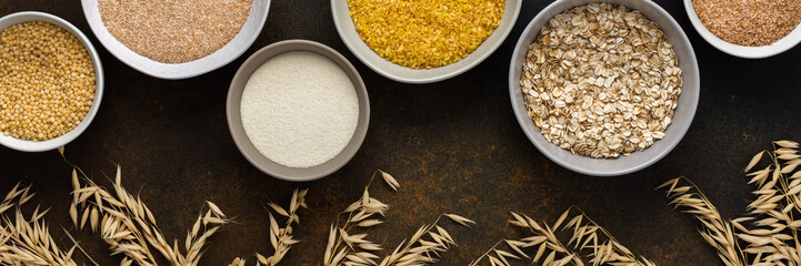 Various grain cereals in bowls banner, top view on a brown background with bowls of cereals and ears of oats