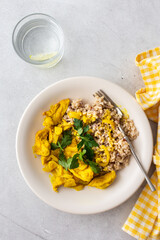 Healthy lunches, brown rice with chicken with turmeric and curry seasoning and fresh herbs, water with lemon, top view on the table