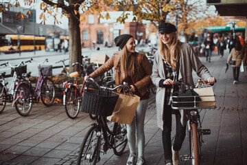 Young women walking on a city street shopping and pushing a bicycle