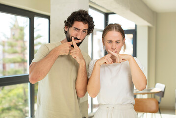 young adult couple looking serious and displeased with both fingers crossed up front in rejection, asking for silence