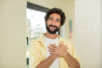 young crazy bearded man feeling romantic, happy and in love, smiling cheerfully and holding hands close to heart