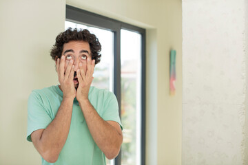 young crazy bearded man feeling shocked and scared, looking bored with hands on cheeks