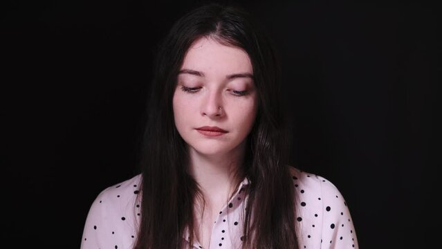 Portrait of a beautiful brunette in a light blouse with polka dots on a black background. Sad girl puts on glasses, then straightens her hair and smiles
