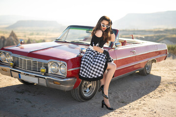 beautiful girl in retro style posing near vintage red cabriolet car.