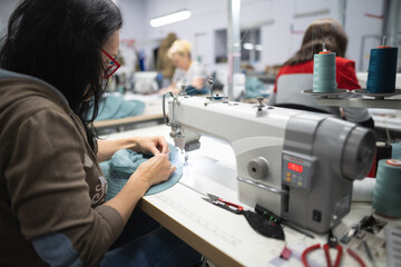workers in an industrial garment factory sew clothes on sewing machine