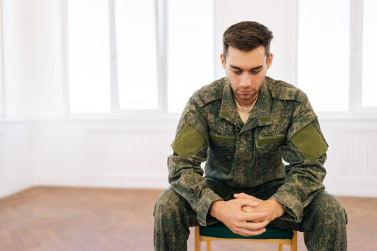 Portrait of frustrated veteran male in camouflage uniform sitting in circle during PTSD group therapy session looking down with pensive expression. Concept of mental health, psychotherapy. - Powered by Adobe