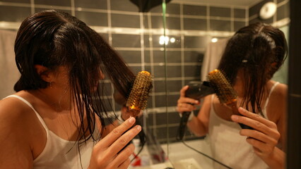 Woman night routine drying and brushing hair in front of bathroom mirror