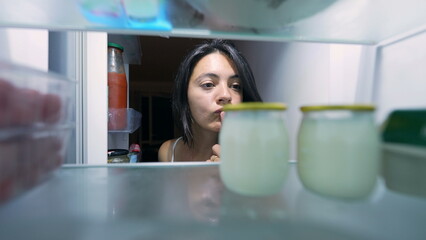 Woman opening fridge and picking yogurt from inside refrigerator