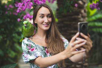 a beautiful girl with a parrot on her shoulder is smiling and taking a selfie © Tsyb Oleh