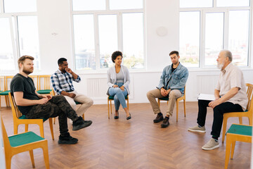 Side remote view of confident mature male coach psychologist talking sitting in circle during group therapy with diverse and different ages people. Concept of group consulting of mental health problem