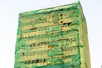 Tall building with bamboo scaffolding, and covered in tattered ripped scaffold netting,  Phnom Penh...
