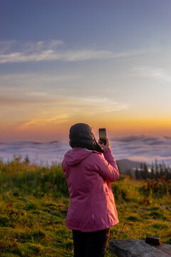landscape in the mountains,sunset,sunrise,a girl looks at the horizon of the sun's rays,takes photos on the phone,social networks,blog,no face from the back,travel,conquering the peaks,tourist,hiking
