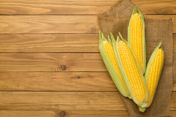 Fresh corn on cobs on wooden background, top view