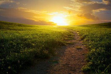 Beautiful mountainous rural landscape; Field panorama with dirt road and cloudy sky at sunset.