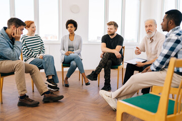 Wide shot of mature male psychotherapist leading therapy meeting with addicted diverse and different ages people sitting in circle during therapy meeting. Concept of consulting mental health problem. - obrazy, fototapety, plakaty