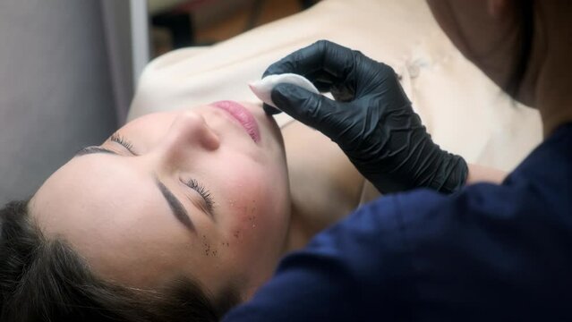 Microblading lip tattoo with a special coloring pigment that corrects the color of the lips in a cosmetology clinic. Hand doing lip cleaning procedure with cotton pad