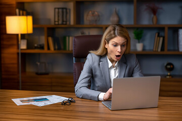 Shocked young business woman using laptop looking at computer screen blown away in stupor sitting...