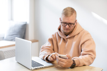 A man works at a computer. Home office, scandinavian minimalist interior. Information Technology. Search for information on the Internet. A man with glasses looks at a laptop screen.