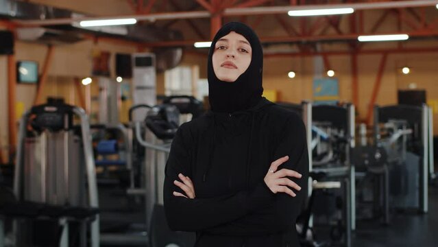 Athletic Muslim Sports Woman Wearing Hijab and Sportswear posing in the gym. Energetic Fit Female Athlete Training in the Gym Alone. Side View