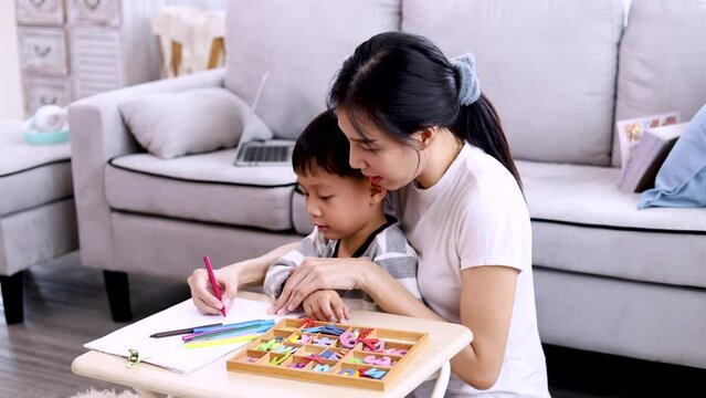 Lifestyle education at home for kids concept, cute boy sitting on mother lap learning how to draw colorful picture with mom, mother cuddling son playing and teaching, motherhood relationship bonding