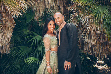 beautiful indian couple smiling with a bindi and traditional sari dress in front of palm fronds...