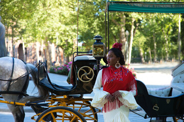 Young black woman dressed as a flamenco gypsy in a famous square in Seville, Spain. She is wearing...