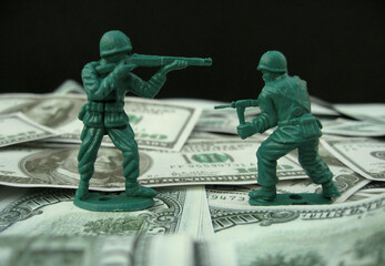 Two toy soldiers fighting over american dollar bills. War concept.