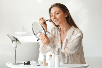 Young woman with mirror and brush applying powder at home