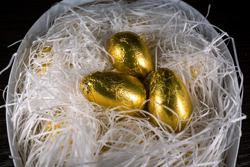 Chocolate Easter eggs in golden cover. Golden eggs in white paper shavings. Candies in the shape of a golden eggs