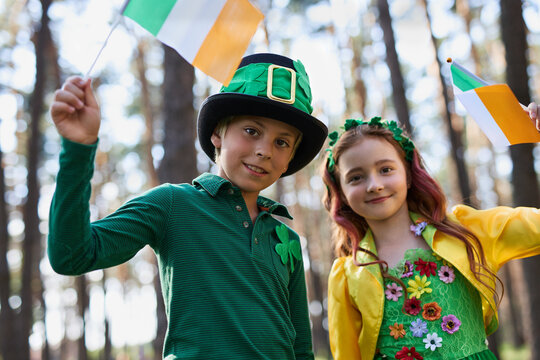 Happy kids celebrating St Patricks Day on the 7th of March. Portrait of cheerful white children dressed in green festival costumes and waving with Irish flags