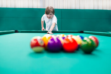 smiling 10 year old boy playing billiards. happy child holding a cue, hitting a billiard ball on a...