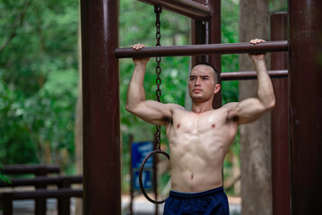 Obraz premium Handsome man exercises by hanging on a bar outdoor, Asian man trains for sporting events