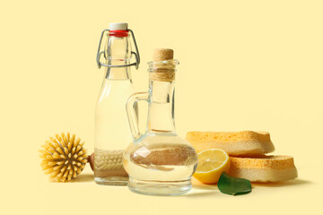 Bottles of vinegar, brushes, sponges and lemon on color background