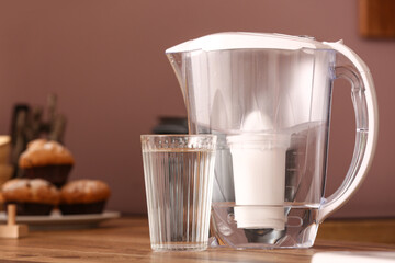 Glass of pure water and filter jug on wooden kitchen counter