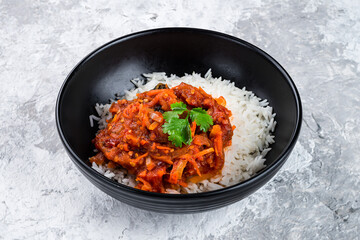 Boiled rice with stewed eggplants, sweet peppers, carrots, tomatoes, onions, sauce and parsley in a bowl.