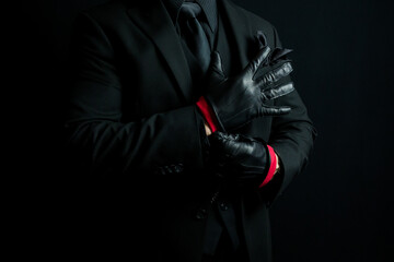 Fototapeta na wymiar Portrait of Mysterious Man in Dark Suit Pulling on Leather Gloves Menacingly. Mafia Hit Man or Violent Gangster.