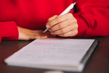 Close-up woman's hand holding a pencil and writing information in a notebook