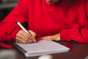 Close-up woman's hand holding a pencil and writing information in a notebook