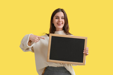Fototapeta na wymiar Female teacher pointing at chalkboard on yellow background