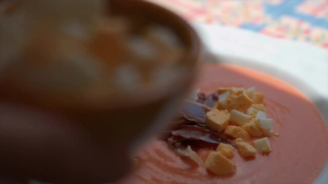 Woman garnishing Salmorejo with boiled egg and jam&oacute;n  as a finishing touch
