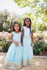 beautiful indian girls sisters smiling with a bindi and traditional sari dress in a garden with flowers