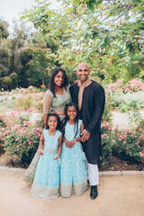 beautiful indian family with daughters girls sisters hugging in close with a bindi and traditional sari dress and kurta in a garden with flowers